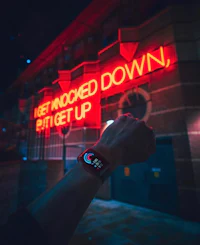 a person holding an apple watch in front of a neon sign