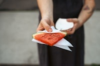 a person holding a piece of watermelon on a piece of paper