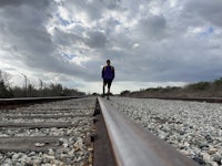 a person walking on a train track under a cloudy sky