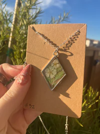 a person holding up a necklace with a flower on it