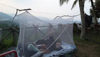 a man sleeping under a mosquito net on top of a hill
