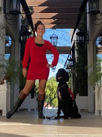 a woman in a red dress posing with a black dog