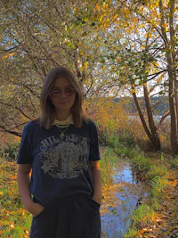 a girl standing in a wooded area near a stream