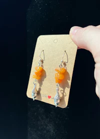 a person is holding a pair of orange dangling earrings