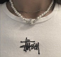 a woman wearing a white t - shirt with a pearl necklace