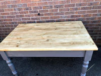 a wooden table with two legs in front of a brick wall