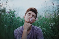 a young man smelling a flower in a field