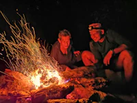 two men sitting around a campfire at night