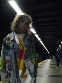 a man in a denim jacket standing in a subway station