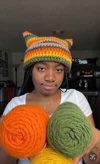 a woman holding up a crocheted hat with different colors of yarn