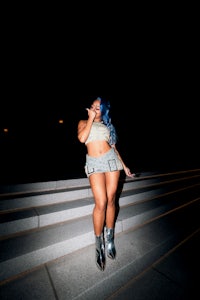 a woman with blue hair standing on steps at night