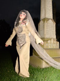 a woman dressed as a bride standing in front of a gravestone