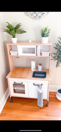a wooden play kitchen with a sink and potted plants