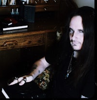a man with long hair sitting in front of a desk