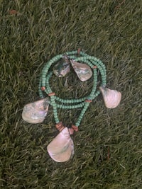 a green necklace with shells and beads on the grass