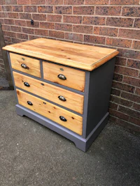 a grey and wood chest of drawers in front of a brick wall