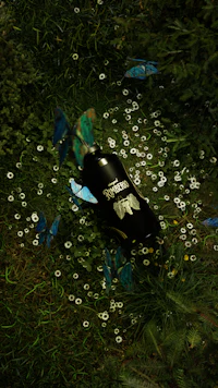 a bottle laying in the grass with butterflies flying around it