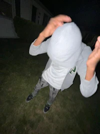 a person in a gray hoodie standing in a yard at night