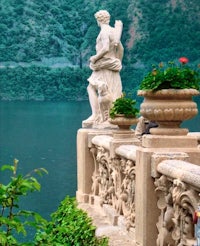 a statue sits on a balcony overlooking a lake