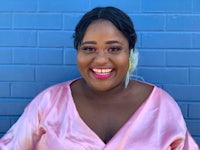 a woman in a pink dress smiling in front of a brick wall