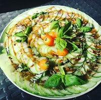 a plate topped with sliced cucumbers, tomatoes and basil