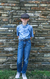 a boy in jeans and a hat standing in front of a stone wall