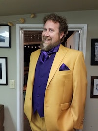 a man wearing a yellow suit and purple tie
