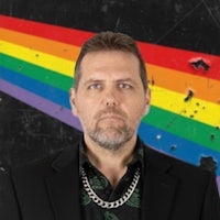 a man in a suit standing in front of a rainbow flag