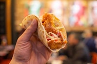 a person holding up a fish taco in a restaurant