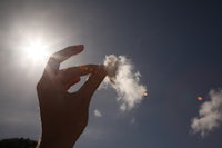 a person's hand is holding a cloud in the sky