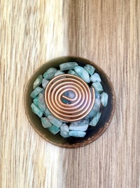 a copper spiral with green stones on top of a wooden table