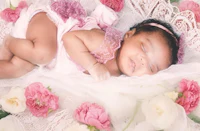 a baby girl is laying on a bed of flowers