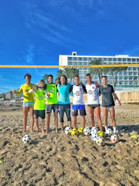 a group of people posing with soccer balls on the beach
