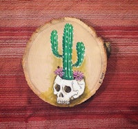 a painting of a cactus and a skull on a slice of wood