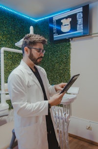 a man in a white coat is looking at a tablet in a dental office