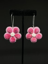 a pair of pink flower earrings on a black stand