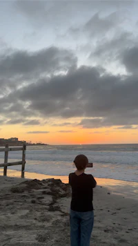 a woman taking a picture of the ocean at sunset