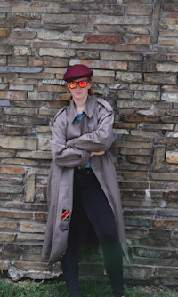 a woman in a trench coat leaning against a wall
