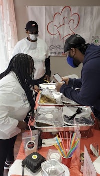 a group of people standing around a table with food on it