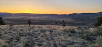 two cowboys standing in a grassy field at sunset