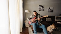 a man playing an electric guitar in a living room with a dog