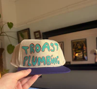 a person holding a hat that says toast plumbing
