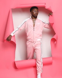 a man in a pink tracksuit posing in front of a pink wall