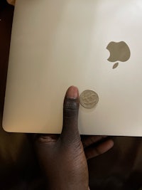 a person holding an apple laptop with a coin on it