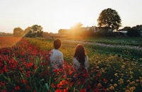 a couple walking through a field of flowers at sunset