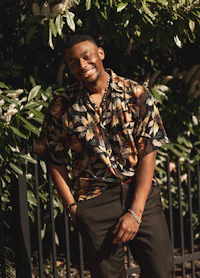a young man wearing a floral shirt and black pants
