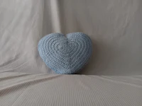 a blue heart shaped crocheted pillow on a bed