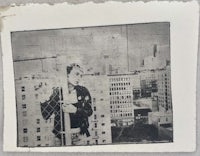 a black and white photograph of a man leaning against a fence