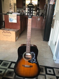 an acoustic guitar sitting on a rug in a kitchen