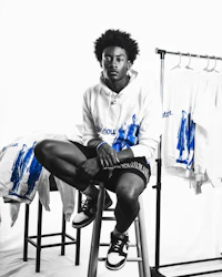 a young man sitting on a stool next to a rack of t - shirts
